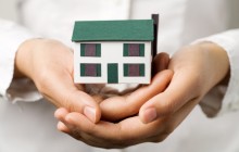 A pair of hands holding a small house. Real estate or insurance concept.